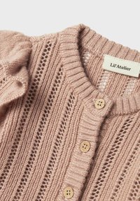 Ljusrosa stickad kofta med ett texturerat m�önster, ribbat krage och träknappar. Taggen med texten "Lil’Atelier" är synlig.