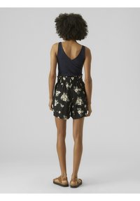 Granatowy top bez rękawów z dekoltem w serek, w zestawieniu z czarnymi szortami w kwiaty, które mają paskową talię i luźny krój. Całość dopełniają beżowe sandały.