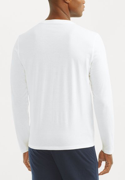 White long-sleeve shirt made from soft fabric, featuring a crew neckline and straight hem, paired with navy shorts. Back view displayed.