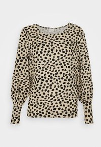 Blouse beige avec des tâches abstraites noires, dotée d'un col rond et de manches longues bouffantes, réalisée en tissu lisse.