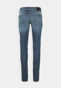 Tummansiniset farkut slim fit -mallilla, joissa on takataskut ja hienovaraisia ompeluyksityiskohtia. Materiaali on kuluneen näköinen mukavuuden takaamiseksi.