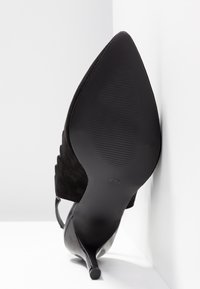 Chaussure noire à talons hauts avec un bout pointu et une tige en daim. Dispose d'une semelle élégante avec un motif texturé pour une meilleure adhérence.