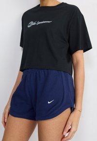 Black cropped t-shirt with white logo and navy blue ribbed shorts featuring a small white Nike swoosh. Smooth fabric, casual fit.