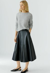 Schwarzer Leder-Midi-Rock mit einer ausgestellten Silhouette, der eine glatte Textur und einen Taillenbund aufweist. Kombiniert mit einem hellgrauen gestrickten Pullover.