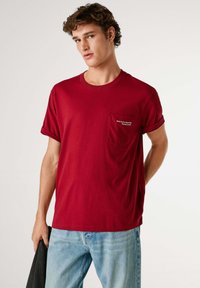 Rood katoenen T-shirt met opgerolde mouwen, voorzien van een borstzak met witte geborduurde tekst. Zachte textuur, comfortabele pasvorm.