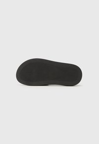 Semelle de chaussure en caoutchouc noire avec un motif de grip texturé, des bords arrondis et une surface plate et lisse. Aucun logo ou détail supplémentaire visible.