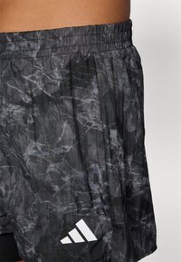 Sorte treningsshorts med et teksturert, abstrakt grått mønster. Elastisk liv med innvendig snor. Har en hvit Adidas-logo på kanten.