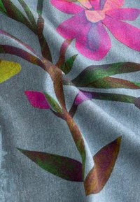 Květinová látka s velkými růžovými květy a zelenými listy na strukturovaném šedém pozadí. Design obsahuje barevné akcenty a detailní prošívání.