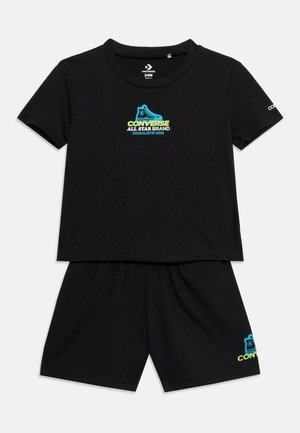 Ensemble deux pièces noir pour tout-petit avec haut à manches courtes et short, arborant le logo de chaussure Converse All Star bleu et jaune sur le devant et la jambe.