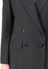 Blazer à rayures noires sombres avec un design croisé, boutons noirs, revers crantés et tissu texturé. Comprend deux poches avant.