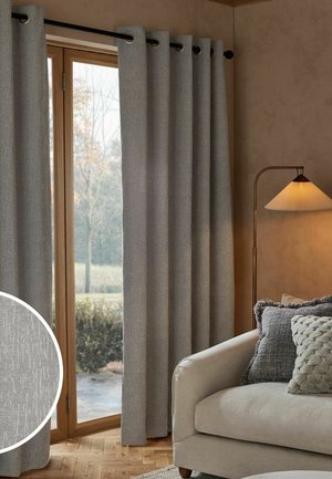 Grau strukturierte Vorhänge, die an einer Stange vor einer Glastür mit Holzrahmen neben einem beigen Sofa mit Kissen und einer Stehlampe hängen.