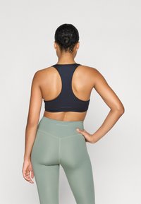 Sujetador deportivo azul marino con diseño de espalda cruzada y textura suave, combinado con legging de talle alto en verde claro con un sutil logo de la marca.