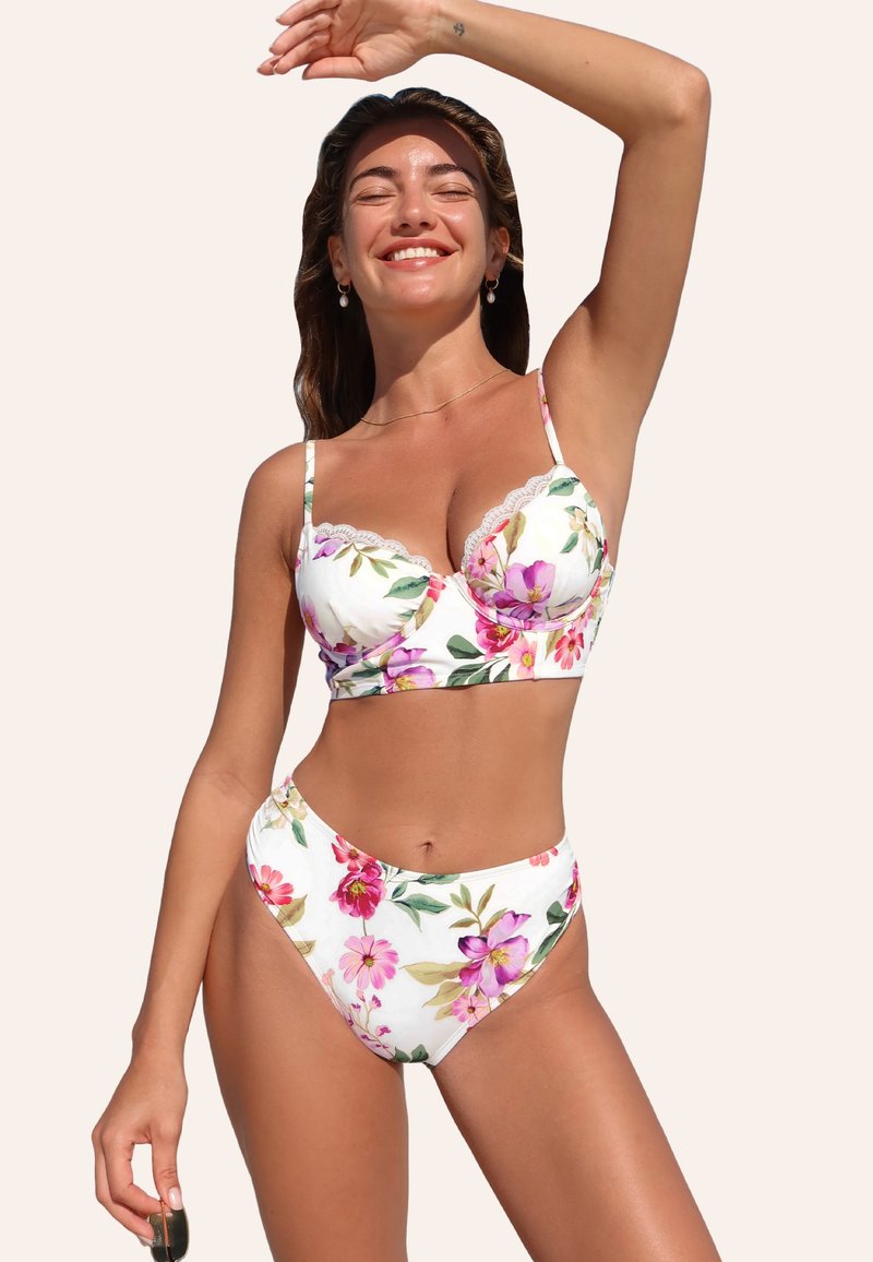 Conjunto de bikini floral con base blanca. Presenta un top tipo balconette con adornos de encaje y braguitas de talle alto, decoradas con flores rosas y verdes.