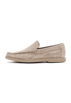 Mocasines de ante beige con un perfil bajo. Presentan un detalle de costura y una suela de goma flexible. Textura suave, diseño minimalista.
