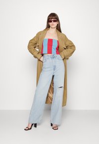 Casaco trinchê bege por cima de um top cropped riscado em azul e vermelho, combinado com jeans de perna larga azul clara com um rasgo no joelho e sandálias pretas de salto alto.