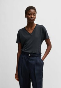 Short-sleeve, dark gray V-neck t-shirt made of soft fabric, paired with high-waisted navy trousers featuring a structured belt and metal accents.
