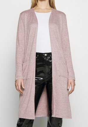 Lungo cardigan rosa realizzato in tessuto morbido, caratterizzato da una vestibilità rilassata, apertura frontale e due tasche anteriori. Abbinato a pantaloni neri lucidi.