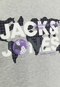 Camiseta de algodón gris con un gráfico de un globo y el texto 'JACK & JONES' en blanco y púrpura, con un patrón de cuadrícula detrás del globo.