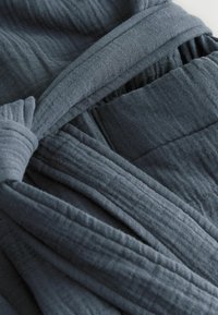 Dunkelgrauer Stoff mit einer weichen, strukturierten Oberfläche. Verfügt über eine verdrehte Schleife und eine Tasche, die geschichtete Falten und einen eleganten Fall präsentieren.