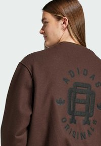 Brun fleece sweatshirt med rund hals, ribbede manchetter og en prægning af logoet på ryggen, suppleret af en sort logoaccent.