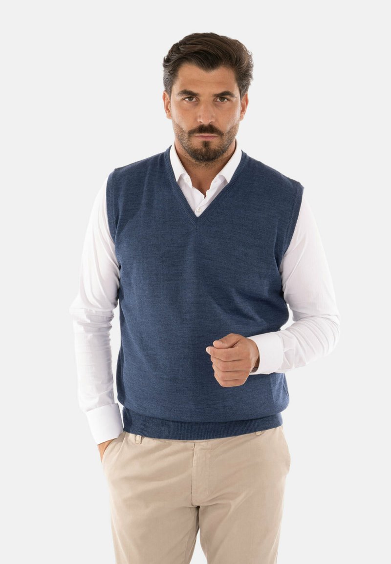 Maglione senza maniche blu navy con scollatura a V, realizzato in materiale a maglia testurizzato, indossato sopra una camicia bianca con colletto, abbinato a pantaloni beige.