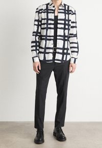 Chemise à motif noir et blanc avec un design en grille, tissu en mélange de coton, devant boutonné, assortie à un pantalon noir et des chaussures.