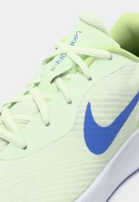 Hellgrüner Nike-Laufschuh mit weißen Schnürsenkeln, blauem Swoosh-Logo und dem Text "Vapor Lite" auf der Zunge.