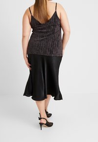 Svart satängkjol med utsvängd nederkant, kombinerad med en texturerad, glittrig mörk topp. Har tunna axelremmar och en draperad ryggdesign.