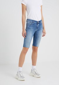 Ljusblå denim bermudashorts med figurnära design, midjeband mitt på höften och uppvikta kanter, kombinerade med vita sneakers och strumpor.