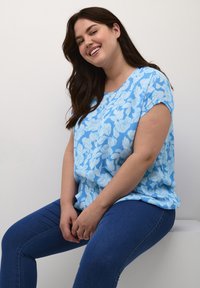 Lyseblå blomstret kortærmet top med en afslappet pasform, der har ribbet struktur og rund halsudskæring, parret med mørkeblå skinny jeans.
