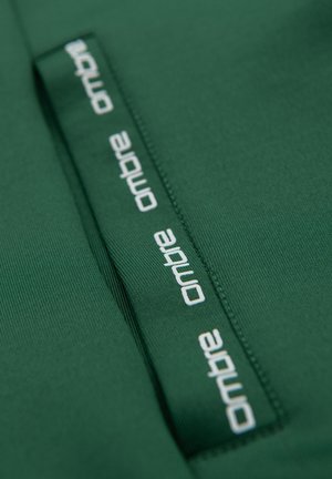 Tela verde con una costura cosida y una tira de tela que presenta el texto blanco repetido "ombre" en una fuente moderna.