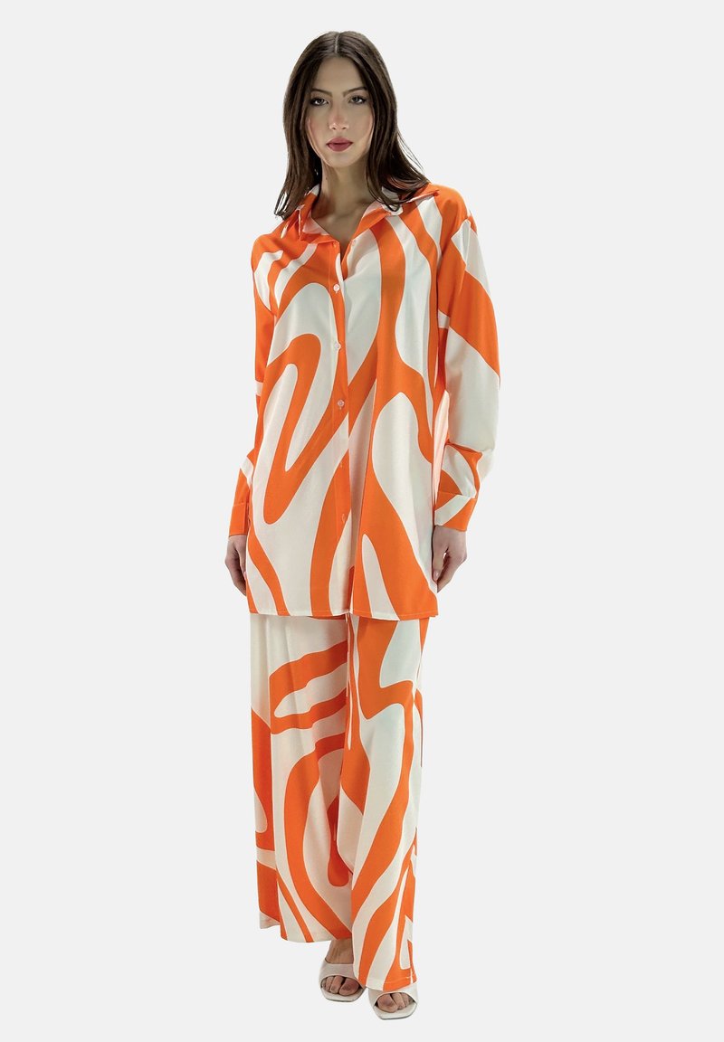 Twee-delige outfit met een oranje en witte draaiende patroon. De stof lijkt lichtgewicht met een ontspannen, vloeiende pasvorm en lange mouwen.