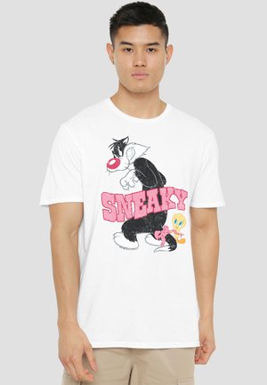 Young man wearing white T-shirt with cartoon characters Sylvester and Tweety and pink text "SNEAKY" on front.