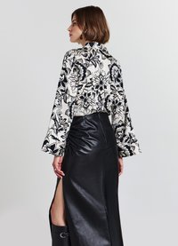 Floral-patterned blouse in black and white, with bell sleeves; paired with a black leather skirt featuring a side slit and ruched detailing.