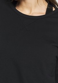 Top negro de manga larga con un cuello redondo, costuras texturizadas y un acabado de tela suave, con un corte holgado y un efecto de capas debajo.