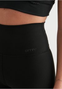 Un sujetador deportivo negro y leggings de cintura alta presentan una textura suave con un logo en la cinturilla, creando un aspecto atlético y elegante.
