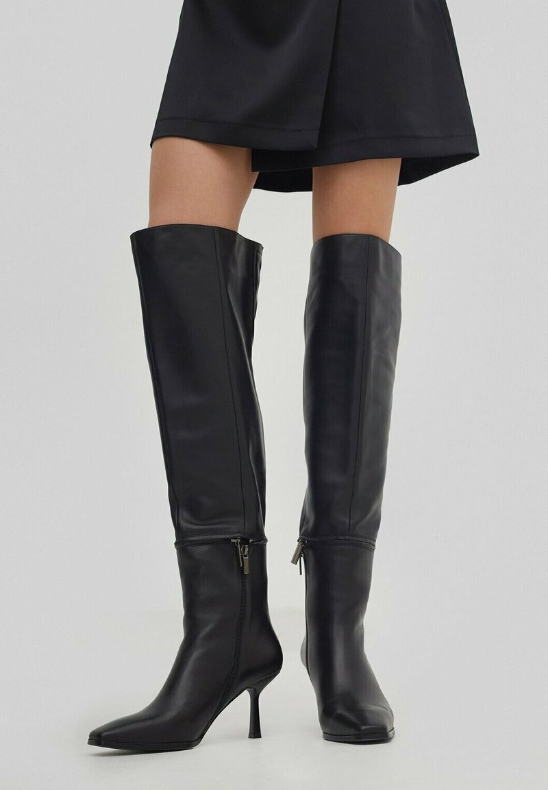 Czarne skórzane botki do kolan z ostrym noskiem i cienkim obcasem typu stiletto. Posiadają zapięcia na zamek przy kostce dla łatwego zakładania.