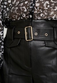 Svart läderbälte med en gyllene rektangulär spänne, med texturerade detaljer, hål och sidofickor.