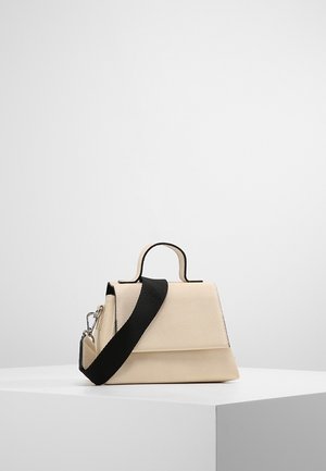 Beige strukturierte Handtasche mit schwarzem verstellbarem Schulterriemen und kleinem Griff, auf einem weißen Sockel vor schlichter Hintergrund.