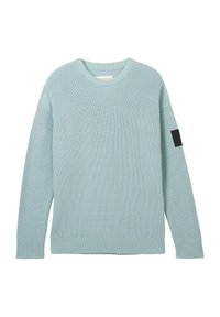 Světle modrý pletený svetr s dlouhými rukávy a kulatým výstřihem, s žebrovaným lemem a manžetami. Na levém horním rukávu se nachází černá nášivka.