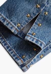 Tissu en denim bleu avec revers pliés, orné de clous en forme d'étoile dorée le long de la couture. Coutures contrastées et texture légèrement délavée.