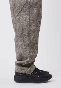 Pantalones grises con un patrón, hechos de tela suave, combinados con zapatillas atléticas negras que tienen suelas texturizadas y acentos reflectantes.