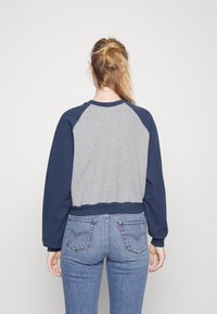 Sudadera gris y azul marino de manga larga, con puños y dobladillo de canalé. Diseño informal con mangas raglán y textura suave.