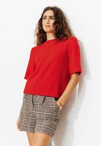 Pull rouge à manches courtes en maille, associé à un short à carreaux. Détails remarquables : une coupe décontractée et un ourlet avec une finition subtile.