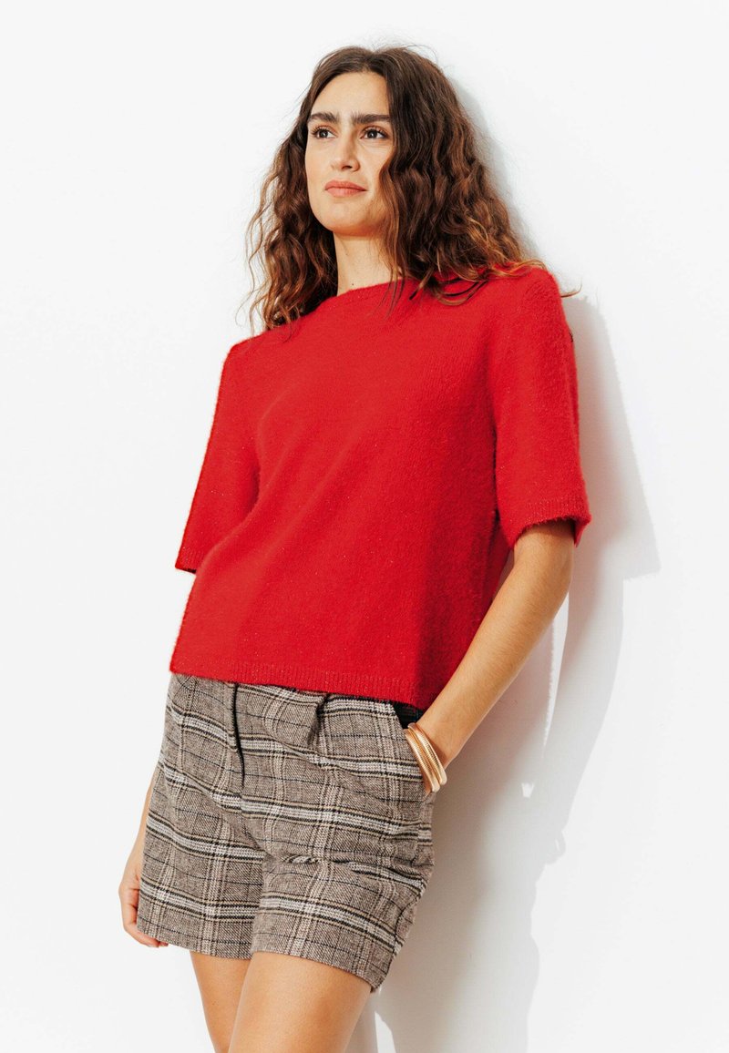 Pull rouge à manches courtes en maille, associé à un short à carreaux. Détails remarquables : une coupe décontractée et un ourlet avec une finition subtile.