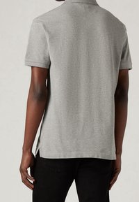 Polo gris à manches courtes, confectionné dans un tissu doux. Il présente un col classique, des fentes latérales à l'ourlet, et un design uni texturé.