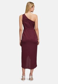 Robe midi bordeaux à une épaule, avec une silhouette ajustée, une texture lisse et une fermeture éclair dissimulée dans le dos. Des escarpins argentés à lanières complètent la tenue.