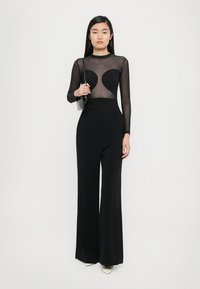 Musthave musträbalt bodysuit, millel on südamekujuga lõiked, millele on lisatud kõrge vöökoht ja laiad mustad püksid ning heledate jalatsitega.