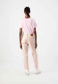 Camiseta rosa claro, jeans rectos color beige con un parche de cuero en la parte trasera y costuras en contraste, combinados con zapatillas altas blancas.