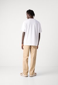 Hvit bomull t-skjorte med avslappet passform, kombinert med beige chinos og joggesko med brune detaljer, sett fra baksiden.